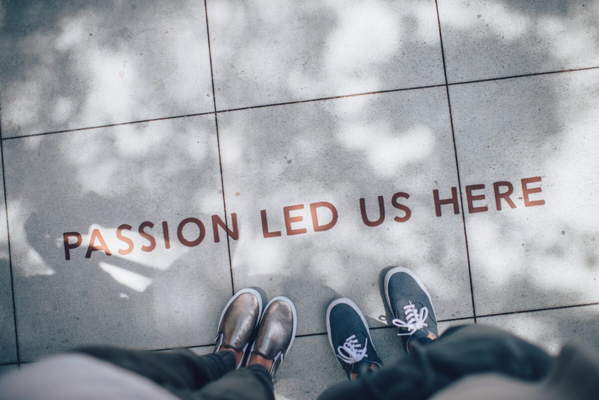 Feet stop at the words "passion led us here" written in brass lettering on the sidewalk